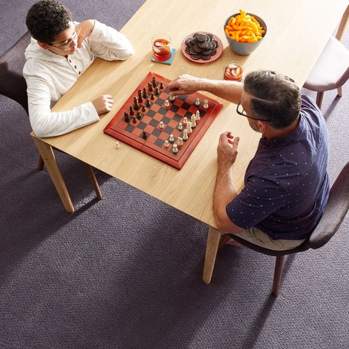 Two people playing chess at a wooden table in a room with purple carpet from B & B Floor Co in Springfield, VA